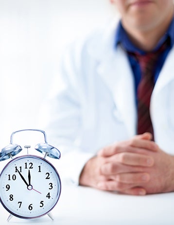 A clock sits on a desk in front of a doctor.